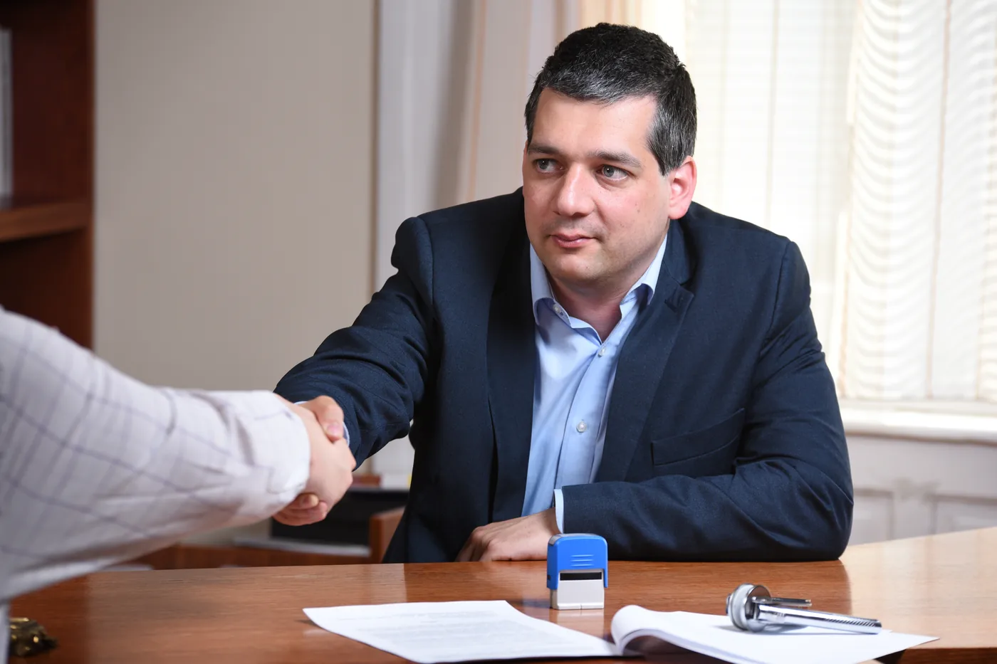 Ügyvéd kezet fog egy ügyféllel, előtérben az aláírt irat és a pecsét